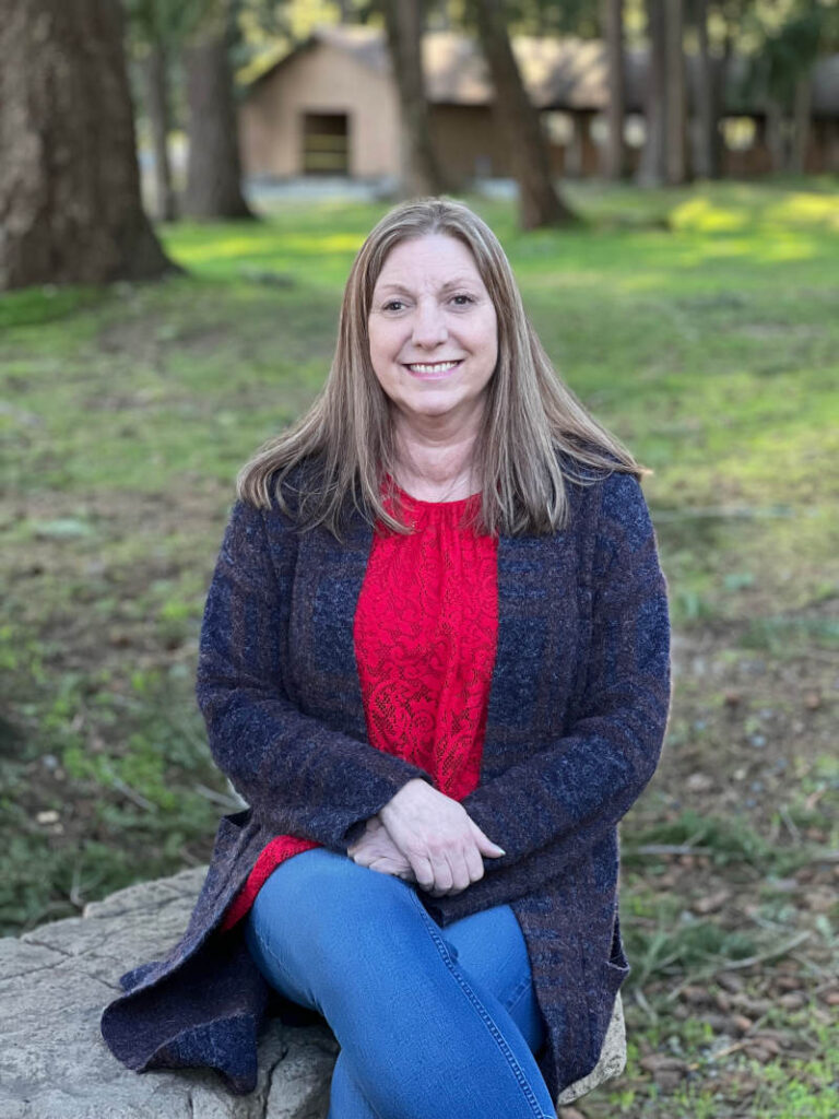 Julie, sitting on a rock, with her hand in her lap, smiling.