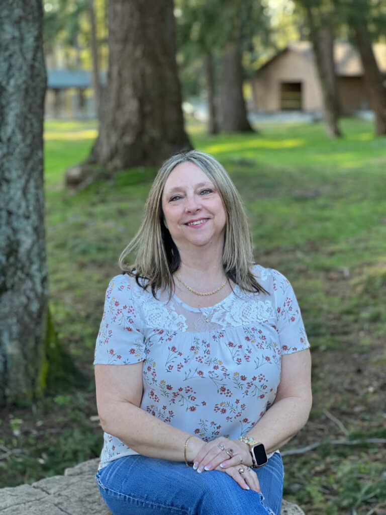 Laura, sitting on a rock, hands in her lap with her head slightly tilted, smiling.